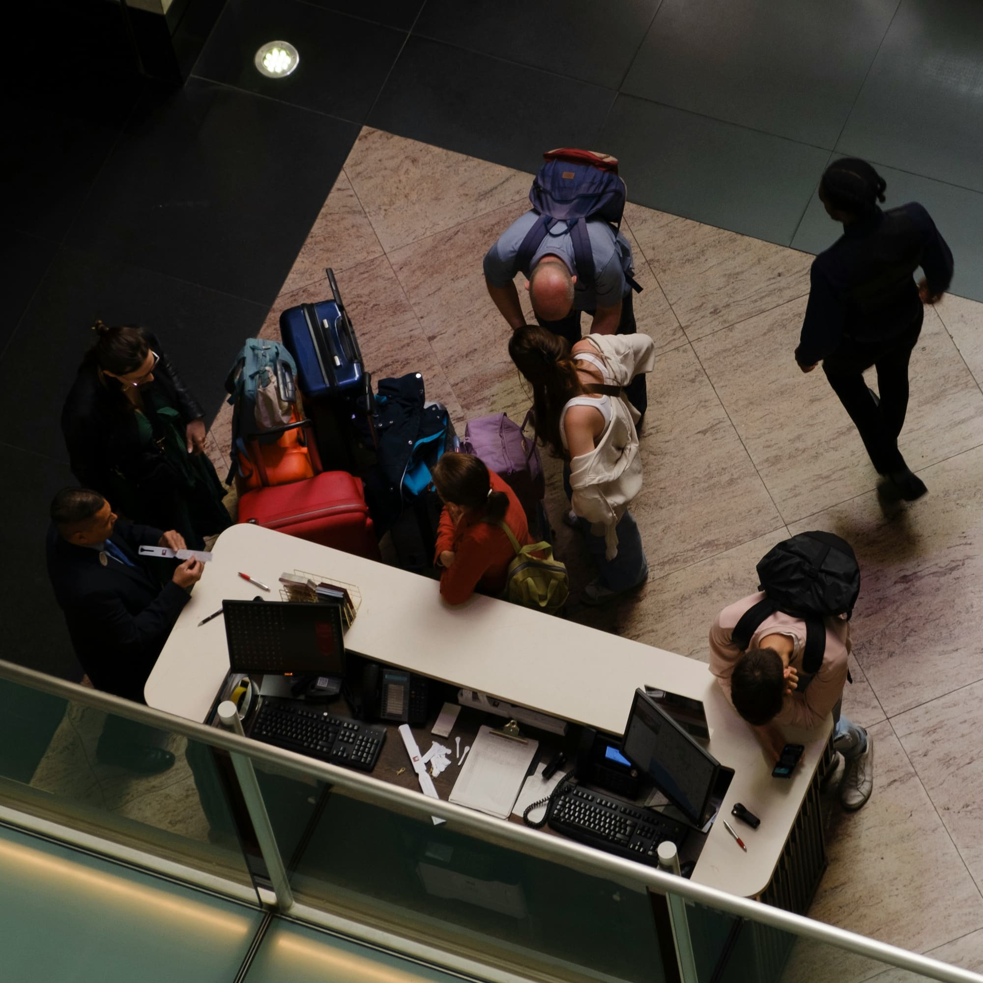 A busy hotel reception desk seen from above, guests with luggage checking in